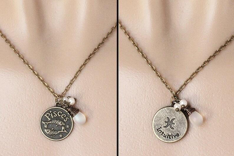 May include: A bronze necklace with a Pisces zodiac charm and the word "Pisces" on the front. The back of the charm has the Pisces symbol and the word "Intuitive". The necklace has two white pearl beads and a white stone hanging from the charm.