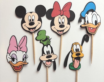 May include: Six cartoon character cupcake toppers featuring Mickey Mouse, Minnie Mouse, Donald Duck, Daisy Duck, Goofy, and Pluto. Each character is a colourful illustration attached to a wooden stick, ideal for decorating cupcakes or other baked goods.