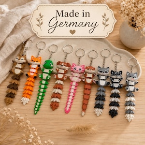 Könnte beinhalten: Eine Sammlung von neun beweglichen Tier-Schlüsselanhängern, darunter Streifenhörnchen, Fuchs, Eidechse, Hund, Axolotl, Otter, Waschbär, Stinktier und Wolf. Jeder Anhänger hat einen beweglichen Schwanz und einen Metallring. Schild: Made in Germany.