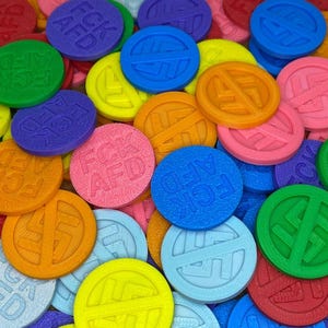 Könnte beinhalten: Eine Ansammlung bunter, runder Token mit dem Text "FCK AFD" und einem durchgestrichenen Symbol. Die Token sind in verschiedenen Farben gehalten, darunter Grün, Blau, Rosa, Orange und Gelb.