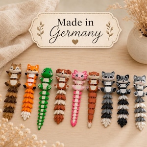 Könnte beinhalten: Eine Sammlung von neun beweglichen Tierfiguren, die in einer Reihe angeordnet sind. Jede Figur hat einen anderen Tierkopf, darunter ein Eichhörnchen, ein Fuchs, eine Eidechse, ein Hund, ein Axolotl, ein Otter und ein Waschbär, mit segmentierten Schwänzen.