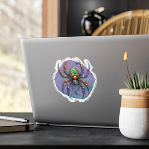 Puede incluir: Una pegatina con un diseño de araña colorida sobre un fondo morado con borde blanco. El texto dice: "I don't do chaos, I engineer it". La pegatina está pegada en un portátil.
