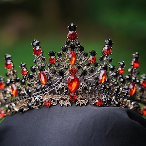 May include: A crown featuring a dark metal filigree base adorned with numerous small black crystals and larger, teardrop-shaped red crystals. The design includes multiple pointed peaks of varying heights, creating a detailed, ornate, and symmetrical structure.