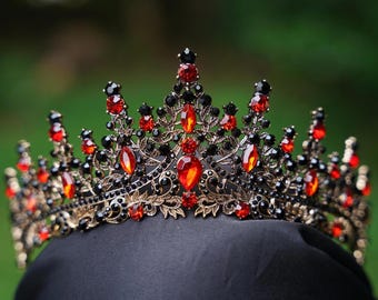 May include: A crown featuring a dark metal filigree base adorned with numerous small black crystals and larger, teardrop-shaped red crystals. The design includes multiple pointed peaks of varying heights, creating a detailed, ornate, and symmetrical structure.