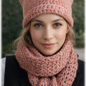 Puede incluir: Un gorro de punto con orejas de gato y una bufanda a juego en tonos melocotón y gris claro. El gorro y la bufanda están hechos de un tejido grueso, perfecto para el frío. El gorro tiene orejas puntiagudas.
