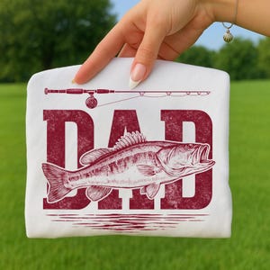 Peut inclure: T-shirt blanc avec un motif rouge. Le motif comprend le mot "DAD", un poisson et une canne &agrave; p&ecirc;che. Le poisson est illustr&eacute; avec la bouche ouverte. Le motif est imprim&eacute; sur un t-shirt blanc.