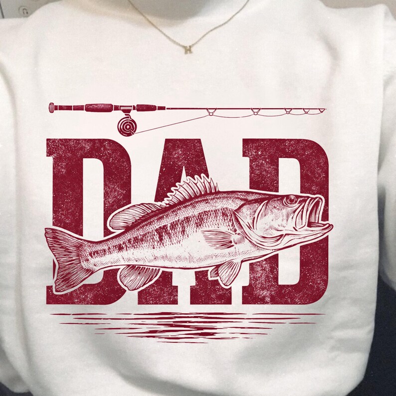 Peut inclure: Sweat-shirt blanc avec un motif rouge repr&eacute;sentant un poisson, une canne &agrave; p&ecirc;che et le mot "DAD". Le poisson est d&eacute;taill&eacute; avec des &eacute;cailles et des nageoires. La canne &agrave; p&ecirc;che est au-dessus du mot "DAD".