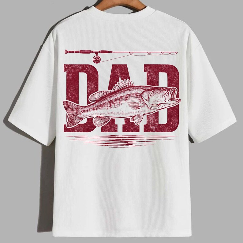 Peut inclure: T-shirt blanc avec un motif rouge repr&eacute;sentant le mot "DAD", un poisson et une canne &agrave; p&ecirc;che. Le motif est centr&eacute; au dos du t-shirt. Le t-shirt a des manches courtes et un col rond.