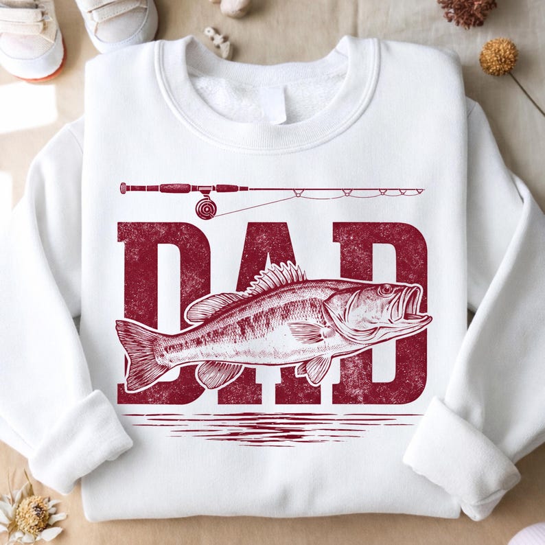 May include: White sweatshirt with a distressed red graphic that says "DAD" with a fish and fishing rod design. The sweatshirt is a crew neck style and is made of a soft material.