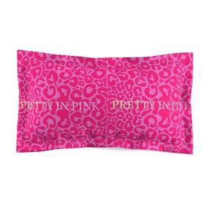 May include: A pink pillowcase with a leopard print pattern in shades of pink. The text "PRETTY IN PINK" is printed in gold across the center of the pillowcase. The pillowcase is rectangular in shape.