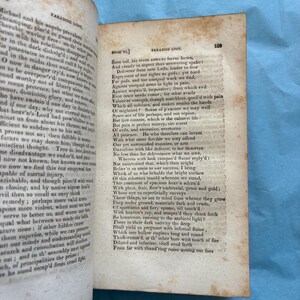 May include: Open book with aged, yellowed pages. Text from "Paradise Lost" by John Milton is visible. The book is open to a page with text on both sides, with the page number 159 visible.