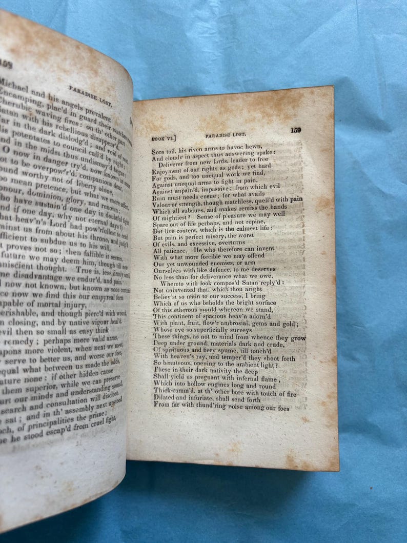 May include: Open book with aged, yellowed pages. Text from "Paradise Lost" by John Milton is visible. The book is open to a page with text on both sides, with the page number 159 visible.