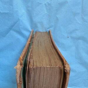 May include: A vintage book with aged, yellowed pages and a worn, brown leather cover. The edges of the cover show signs of wear and tear, with the spine slightly damaged. The book's pages are tightly bound, suggesting it is a hardcover edition.