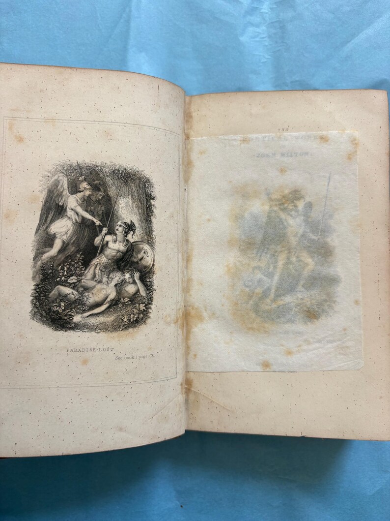 May include: Open book with illustrations from "Paradise Lost" by John Milton. The left page features a detailed engraving of figures with spears and wings. The right page has a faded illustration. The book's pages are aged with visible wear.