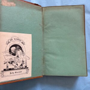 May include: Open vintage book with a brown cover and green interior pages. A small, illustrated bookplate with the text "Ex Libris" and the name "Judy Sherman" is visible. The book shows signs of age.