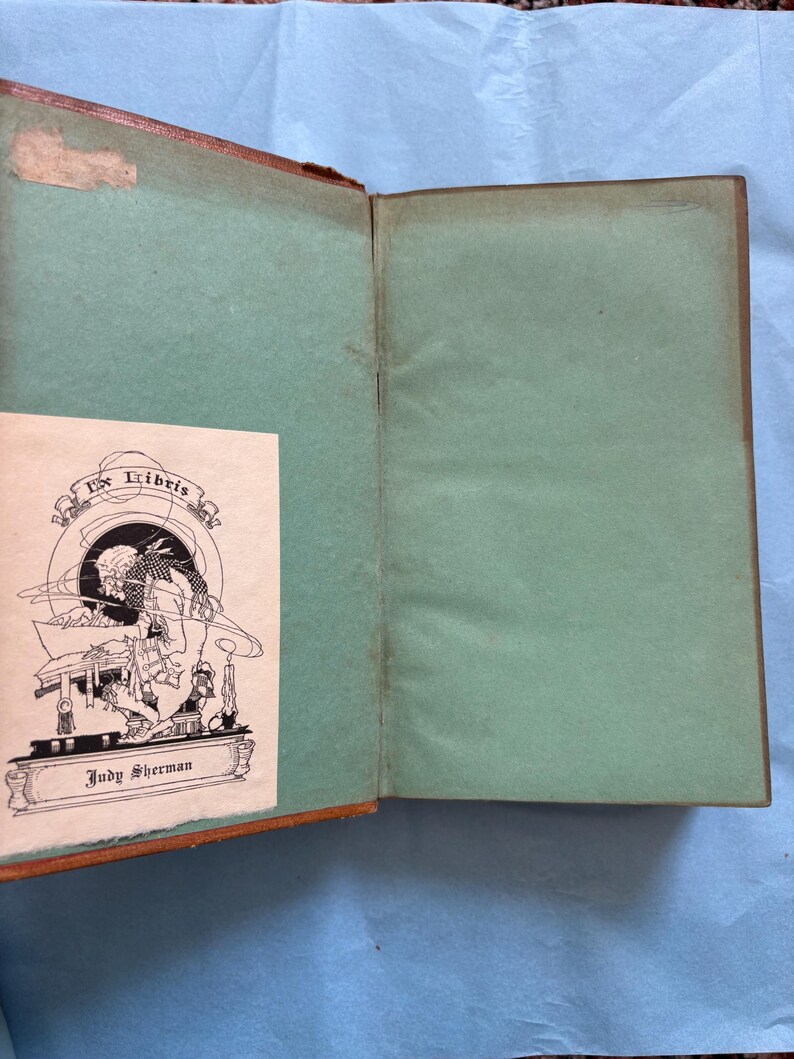 May include: Open vintage book with a brown cover and green interior pages. A small, illustrated bookplate with the text "Ex Libris" and the name "Judy Sherman" is visible. The book shows signs of age.