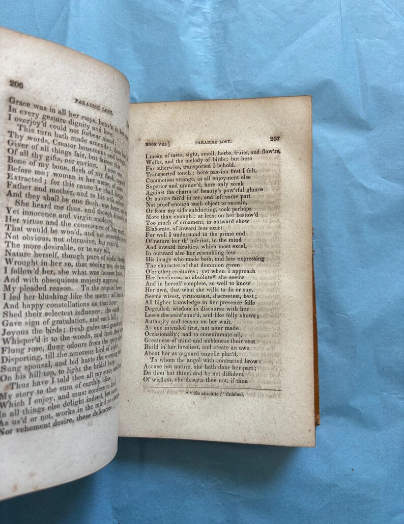 May include: Open book with aged pages, featuring text from "Paradise Lost" by John Milton. The pages are yellowed with age, and the text is printed in a classic serif font. The book is open to a double-page spread, with text filling both sides.