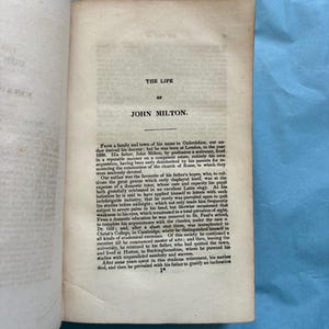 May include: An open book with the title "THE LIFE OF JOHN MILTON" printed at the top of the page. The text is in black ink on aged, off-white paper. The book is slightly open, revealing the text of the biography.