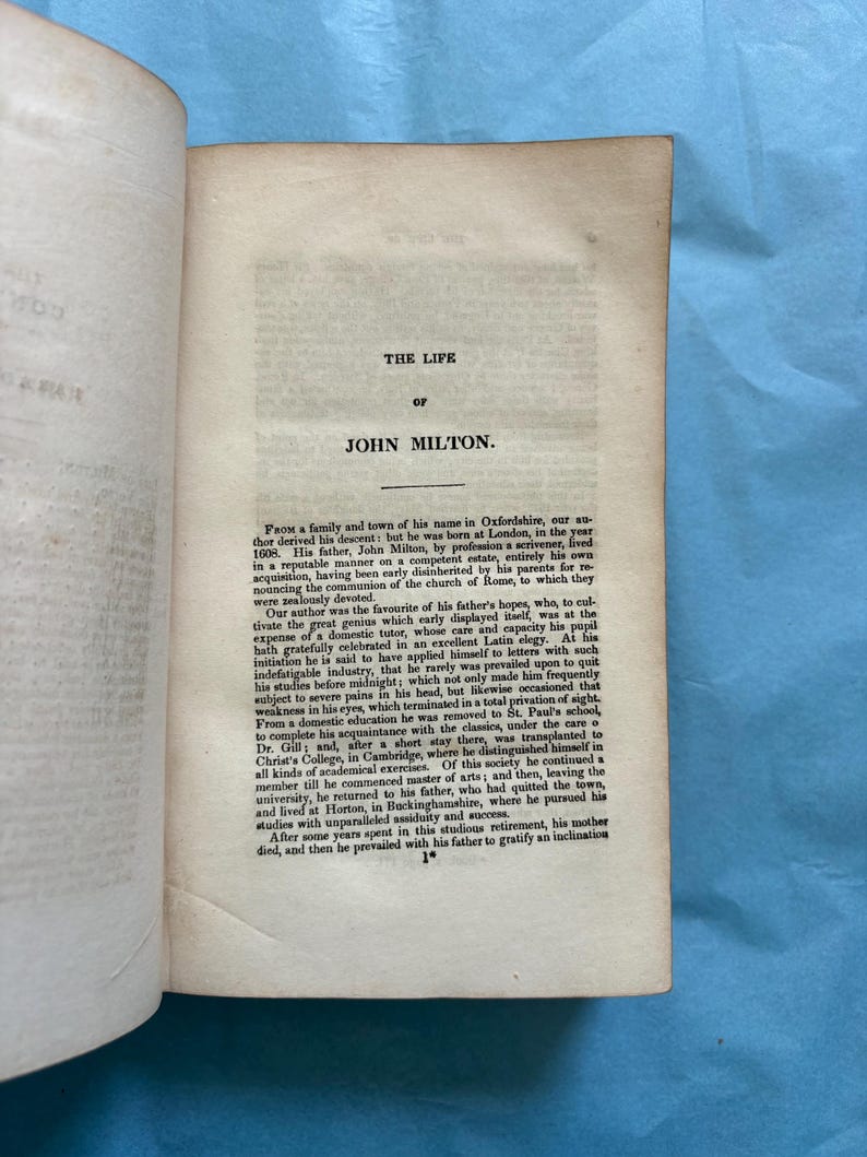 May include: An open book with the title "THE LIFE OF JOHN MILTON" printed at the top of the page. The text is in black ink on aged, off-white paper. The book is slightly open, revealing the text of the biography.