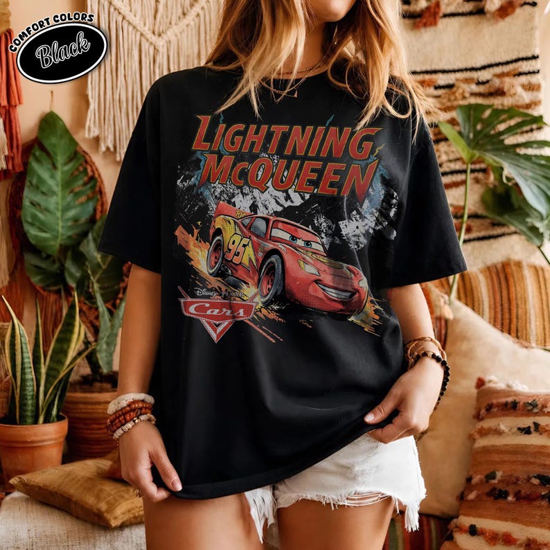 Peut inclure: Un t-shirt noir &agrave; manches courtes avec une impression graphique de la voiture de course rouge Flash McQueen du film Cars. Le texte Lightning McQueen est imprim&eacute; en grandes lettres rouges au-dessus de la voiture, avec le logo Cars en dessous.