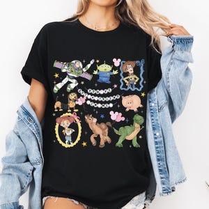 May include: Black t-shirt featuring a colorful graphic of characters from the animated movie Toy Story. The design includes Buzz Lightyear, Woody, and other characters, with the text "You've Got a Friend in Me".