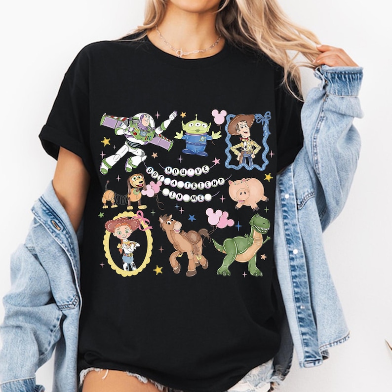 May include: Black t-shirt featuring a colorful graphic of characters from the animated movie Toy Story. The design includes Buzz Lightyear, Woody, and other characters, with the text "You've Got a Friend in Me".
