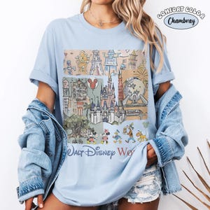 May include: A light blue t-shirt featuring a graphic print of Walt Disney World landmarks and characters. The design includes a castle, a sphere, and various cartoon figures. The text Walt Disney World is printed at the bottom of the graphic.