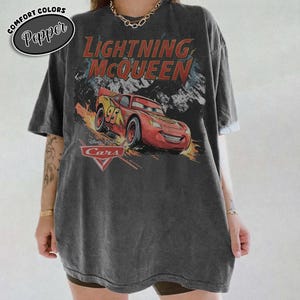 Peut inclure: Un t-shirt gris anthracite &agrave; manches courtes avec une impression graphique de la voiture de course rouge Flash McQueen du film Cars. Le texte Lightning McQueen appara&icirc;t en rouge au-dessus de la voiture, avec le logo Cars et le num&eacute;ro 95.
