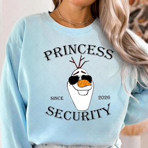 以下が含まれることがあります： 「PRINCESS SECURITY」の文字とサングラスをかけたオラフのイラストが描かれた、水色のスウェットシャツ。「SINCE 2026」の文字も含まれています。スウェットシャツはクルーネックです。