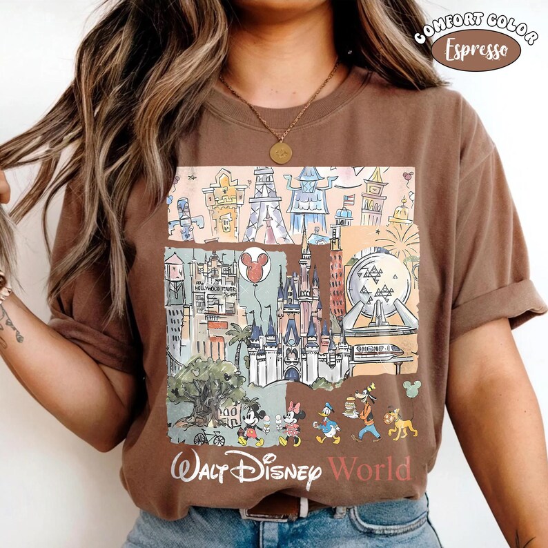 May include: An espresso brown t-shirt featuring a graphic print of various theme park landmarks, including a castle, a geodesic sphere, and a tower. The design includes cartoon characters walking at the bottom and the text Walt Disney World.
