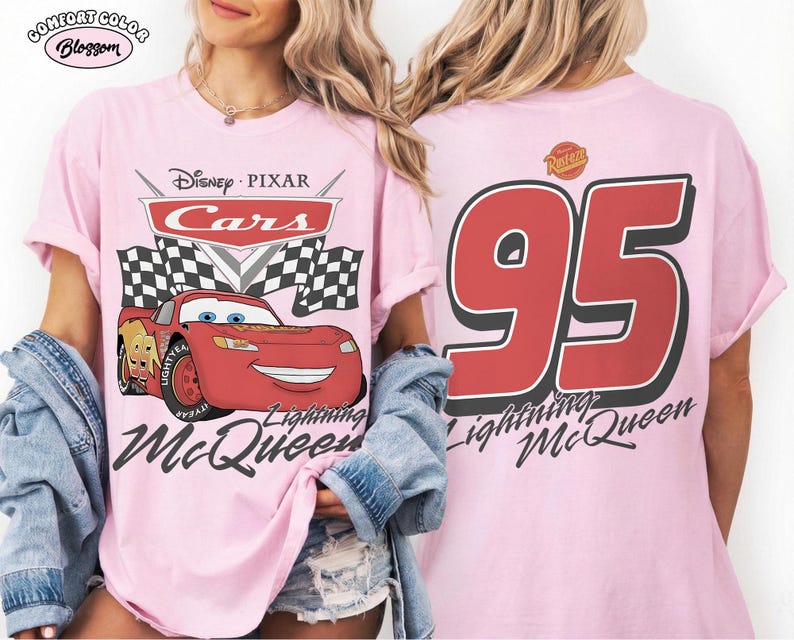 May include: A light pink t-shirt featuring a Disney Pixar Cars graphic on the front with Lightning McQueen, checkered flags, and the text Lightning McQueen. The back displays a large red number 95 with the text Lightning McQueen below it.