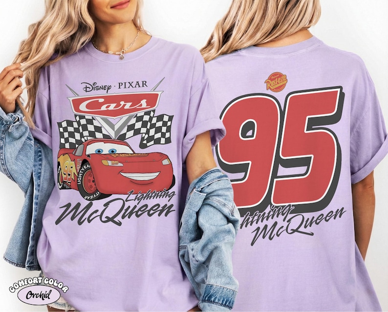 May include: A light purple t-shirt featuring a Disney Pixar Cars graphic on the front with Lightning McQueen, checkered flags, and the text Lightning McQueen. The back displays a large red number 95 with the text Lightning McQueen below it.