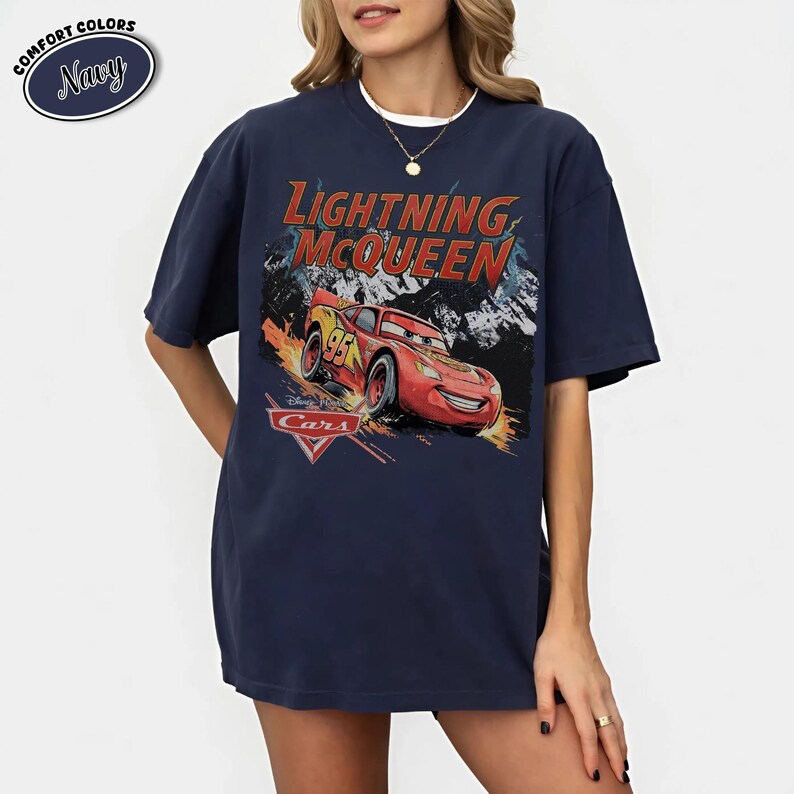Peut inclure: Un t-shirt bleu marine &agrave; manches courtes avec une impression graphique du personnage Flash McQueen du film Cars. Le texte indique Lightning McQueen et Cars. Le t-shirt pr&eacute;sente une encolure ronde, une coupe d&eacute;contract&eacute;e et une &eacute;tiquette Comfort Colors.