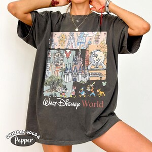 May include: A charcoal gray short-sleeve t-shirt featuring a graphic print of Walt Disney World landmarks and characters including Mickey Mouse, Minnie Mouse, Donald Duck, Goofy, and Pluto. The text Walt Disney World is printed below the graphic.