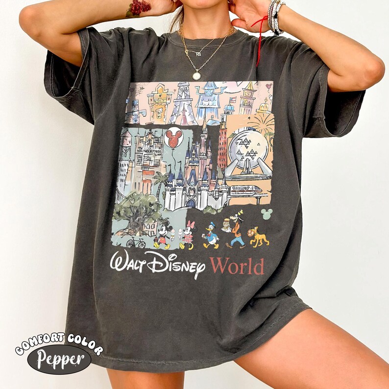 May include: A charcoal gray short-sleeve t-shirt featuring a graphic print of Walt Disney World landmarks and characters including Mickey Mouse, Minnie Mouse, Donald Duck, Goofy, and Pluto. The text Walt Disney World is printed below the graphic.