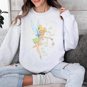 May include: A light gray sweatshirt featuring a cartoon image of Tinkerbell with blue wings and a green dress. The text "All You Need Is Faith, Trust, And Pixie Dust" is written in a whimsical font.