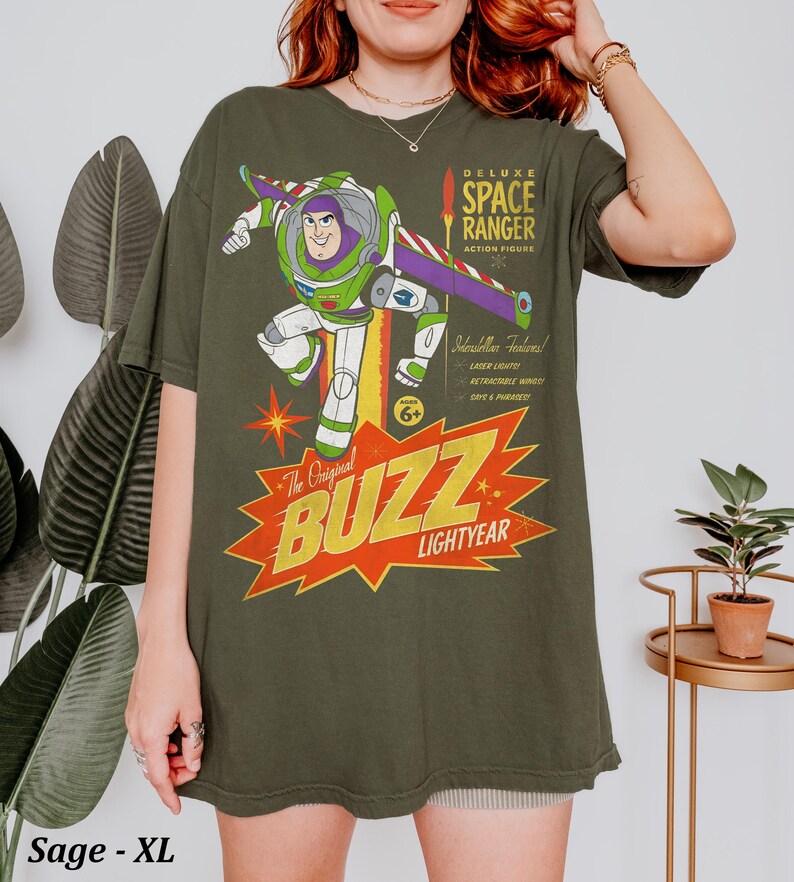 Puede incluir: Una camiseta verde salvia con un gr&aacute;fico de Buzz Lightyear y el texto Deluxe Space Ranger Action Figure y The Original Buzz Lightyear. El dise&ntilde;o incluye una lista de caracter&iacute;sticas como laser lights y retractable wings, junto a una estrella amarilla.