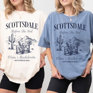 May include: Two t-shirts, one cream and one blue, with a graphic design. The design includes the text "SCOTTSDALE Before The Veil" above a cactus, mountains, and cocktails. Below, it reads "Olivia's Bachelorette SEPTEMBER 2026".