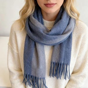May include: A blue and gray scarf with fringe. The scarf is draped around the neck and shoulders. The scarf is made of a soft material and has a gradient color pattern.