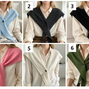 May include: A collection of six knit sweater scarves in light blue, dark gray, black, pink, cream, and olive green. Each scarf features a single button closure and is draped over a cream-colored collared button-down shirt.