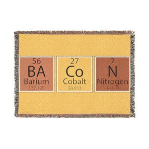 May include: A mustard yellow throw blanket with a fringed edge. The blanket displays three squares with the periodic table elements: Barium (Ba), Cobalt (Co), and Nitrogen (N). Atomic numbers and weights are shown.