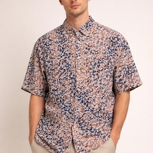 May include: Short-sleeved button-down shirt with a floral pattern in navy blue, white, and orange. The shirt is paired with khaki-colored pants. The model is standing with hands in pockets.