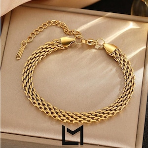 May include: A gold-coloured bracelet with a woven chain design. The bracelet has a lobster clasp and an adjustable chain. The image includes the logo for L'ÉMET MARCHE.
