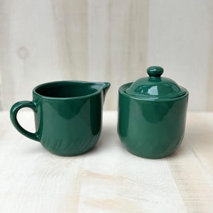 May include: A set of three ceramic mugs with a speckled, cream-colored glaze. Each mug features a different hand-painted floral design in shades of blue, green, and yellow. The mugs have a simple, rounded shape and a comfortable handle.
