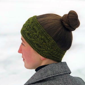 Puede incluir: Una diadema de punto verde con un patrón de trenza. La diadema la lleva una persona con el pelo castaño recogido en un moño.
