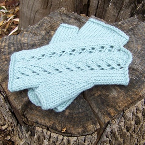 May include: A pair of light blue knitted fingerless gloves with a lacy pattern. The gloves are laid out on a tree stump.