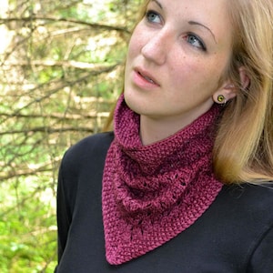 May include: A woman wearing a maroon knitted scarf with a lacy pattern. The scarf is tied around her neck and the ends are hanging down her chest. She is wearing a black shirt and has long blonde hair.