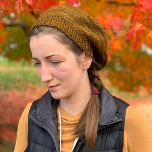 May include: A woman wearing a brown knitted beret with a ponytail and a black vest over a yellow shirt.