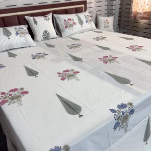 May include: White bedsheet set with floral and leaf patterns in pink, blue, and gray. The set includes a bedsheet and several pillowcases. The bedsheet has a repeating pattern of stylized leaves and floral bouquets.