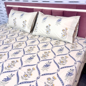 May include: White bed linen set featuring a blue and yellow floral design. The pattern includes a repeating floral motif with blue stems and yellow flowers on a white backdrop. Pillowcases have a striped border. Metric measurements.